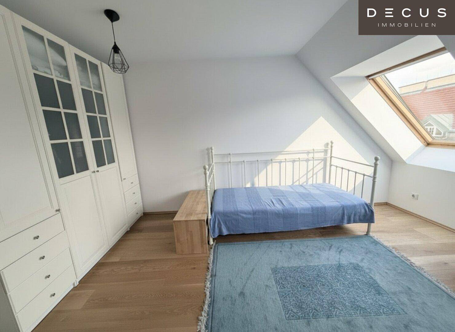 Helles Schlafzimmer mit Holzboden, weißem Bett und großem Dachfenster, das den Raum erhellt.