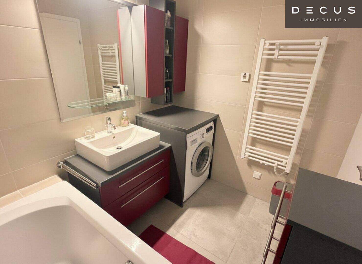 Modernes Badezimmer mit Badewanne, Waschbecken und integrierter Waschmaschine, hell gefliest.