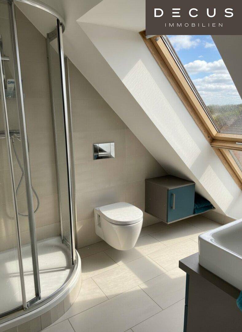 Modernes Badezimmer mit Dusche, wandhängendem WC und Dachfenster, in hellen Fliesen gehalten.