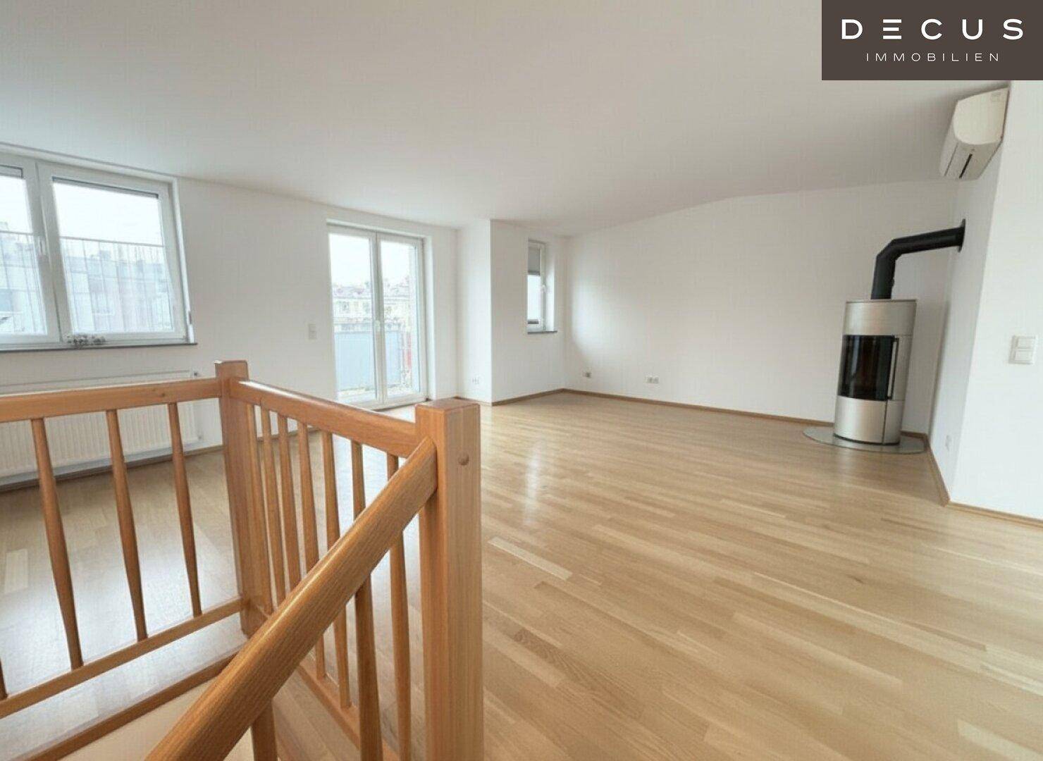 Geräumiger Wohnbereich mit Holzboden, Kaminofen und Zugang zu einem Balkon, unter Dachschrägen gelegen.