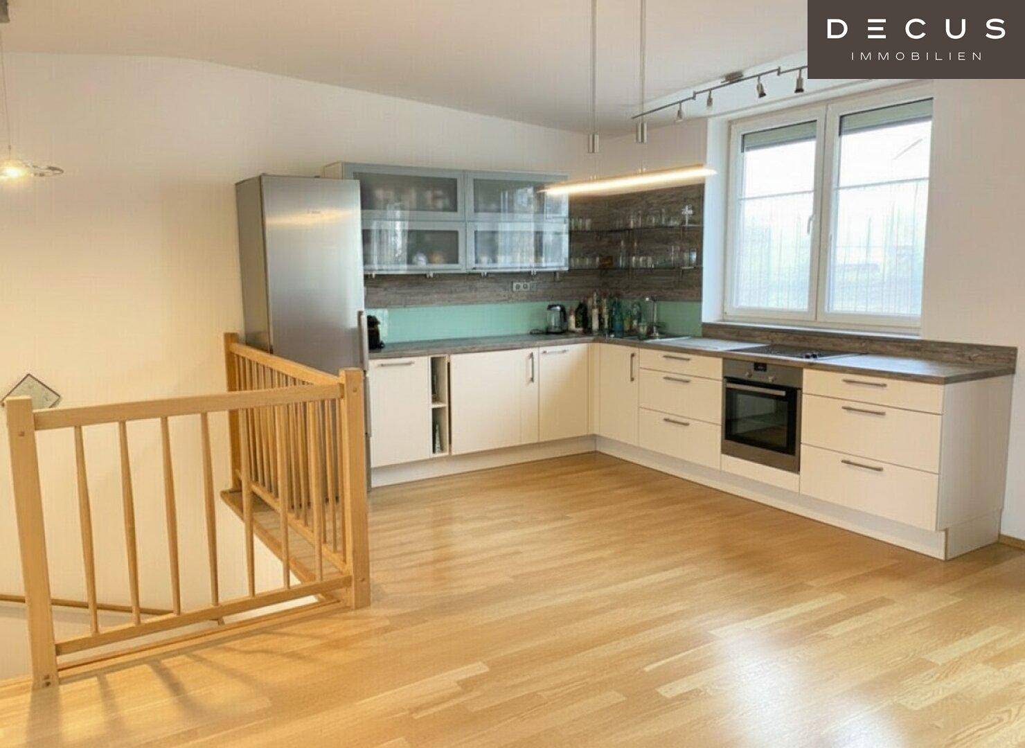 Moderne Einbauküche mit hellen Schränken, Holztheke und integrierten Geräten, offen zum Wohnbereich.