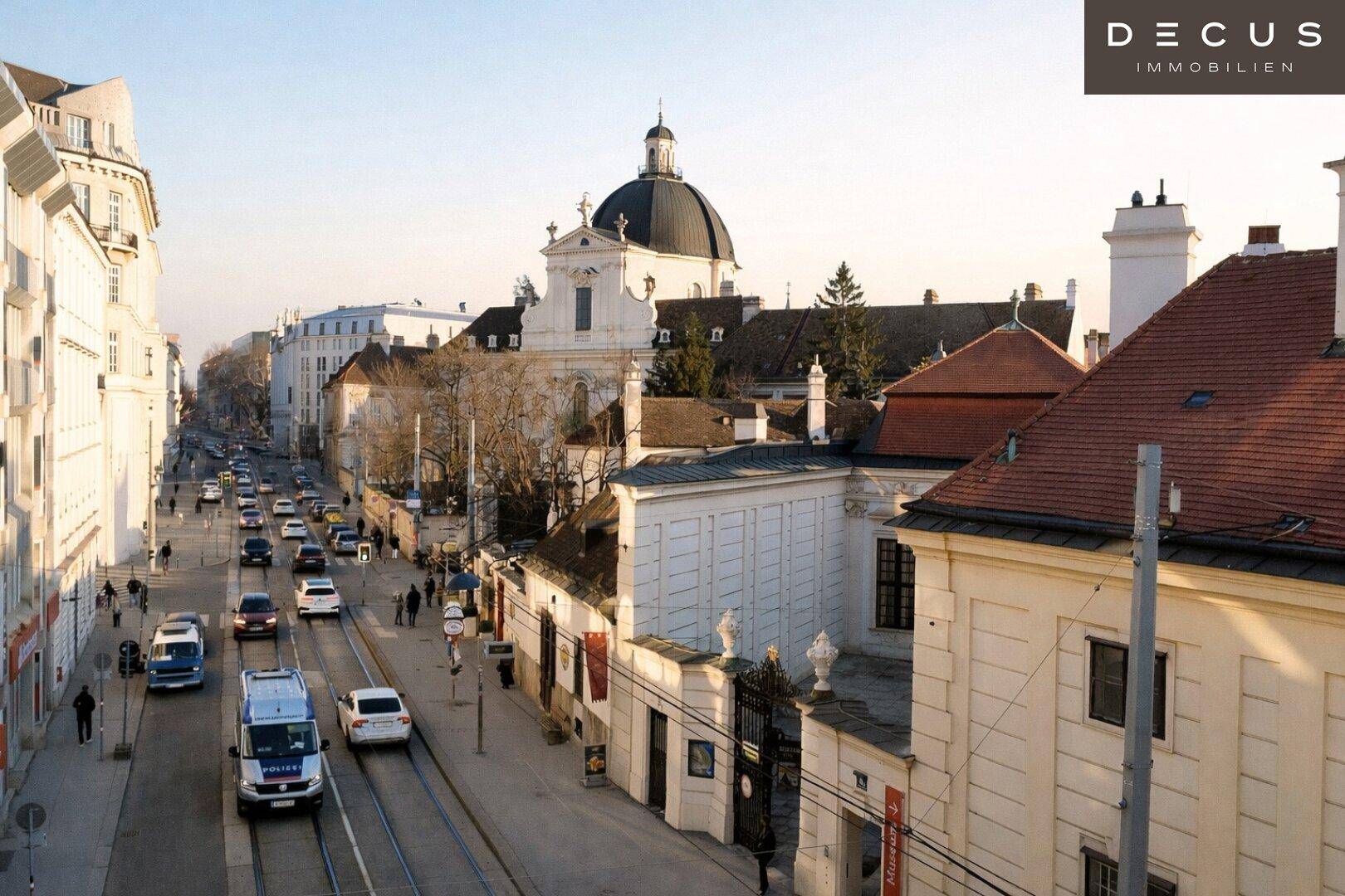 Belebte Stadtstraße mit historischen Gebäuden, Straßenbahn und Blick auf eine Kirche.
