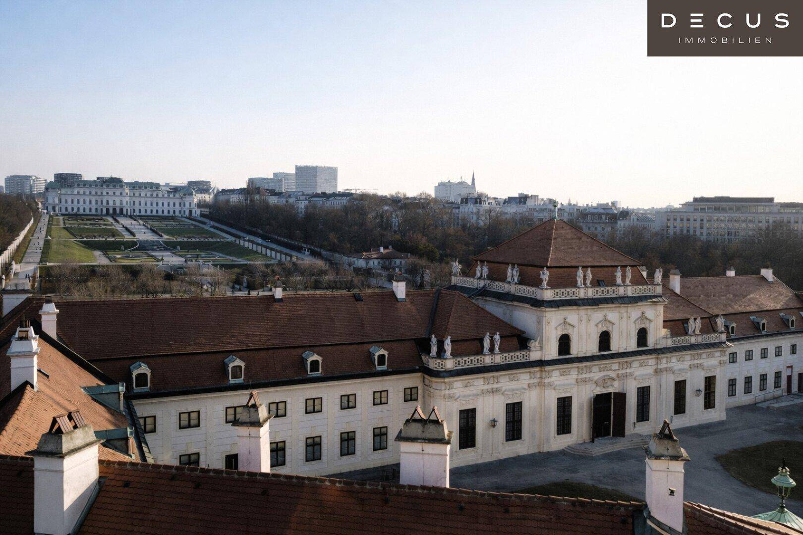 Luftaufnahme eines historischen Schlosses mit weitläufigem Park und Stadtpanorama im Hintergrund.
