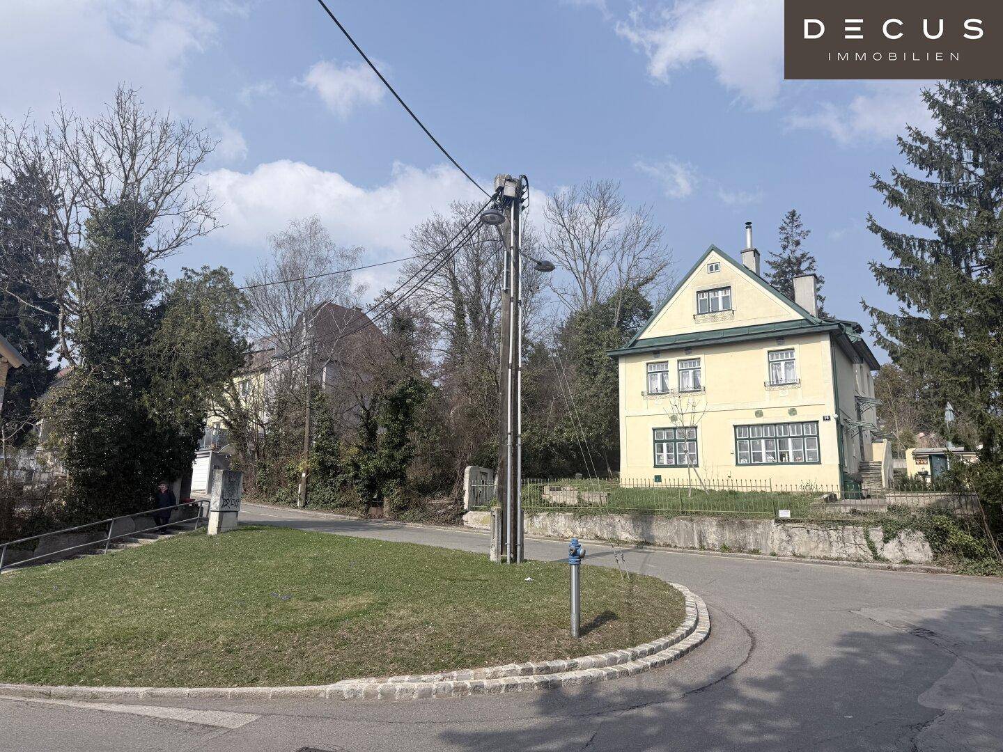 Blick auf eine Straße mit einem gelben Haus auf der rechten Seite und bewachsenen Hängen links.
