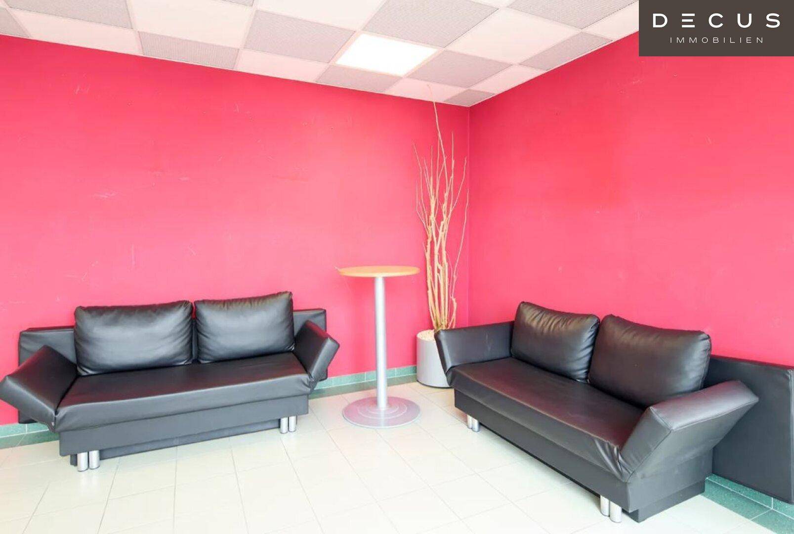 Gemütlicher Loungebereich mit zwei schwarzen Sofas, einem Stehtisch und einer auffälligen roten Wand.