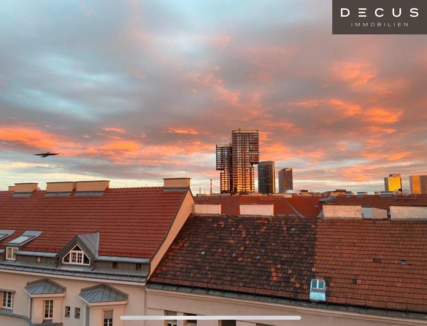 Weitblick über die Dächer der Stadt mit modernen Hochhäusern im Hintergrund bei Sonnenuntergang.