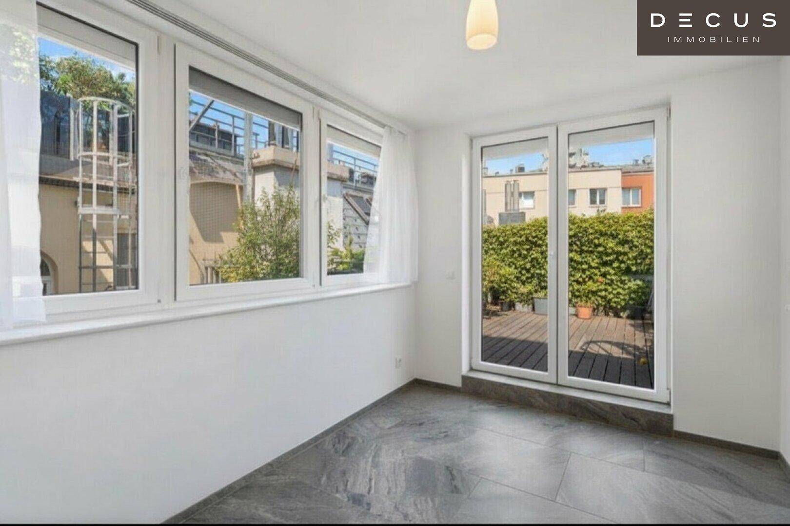 Heller, unmöblierter Raum mit großen Fenstern und Zugang zu einer Terrasse.
