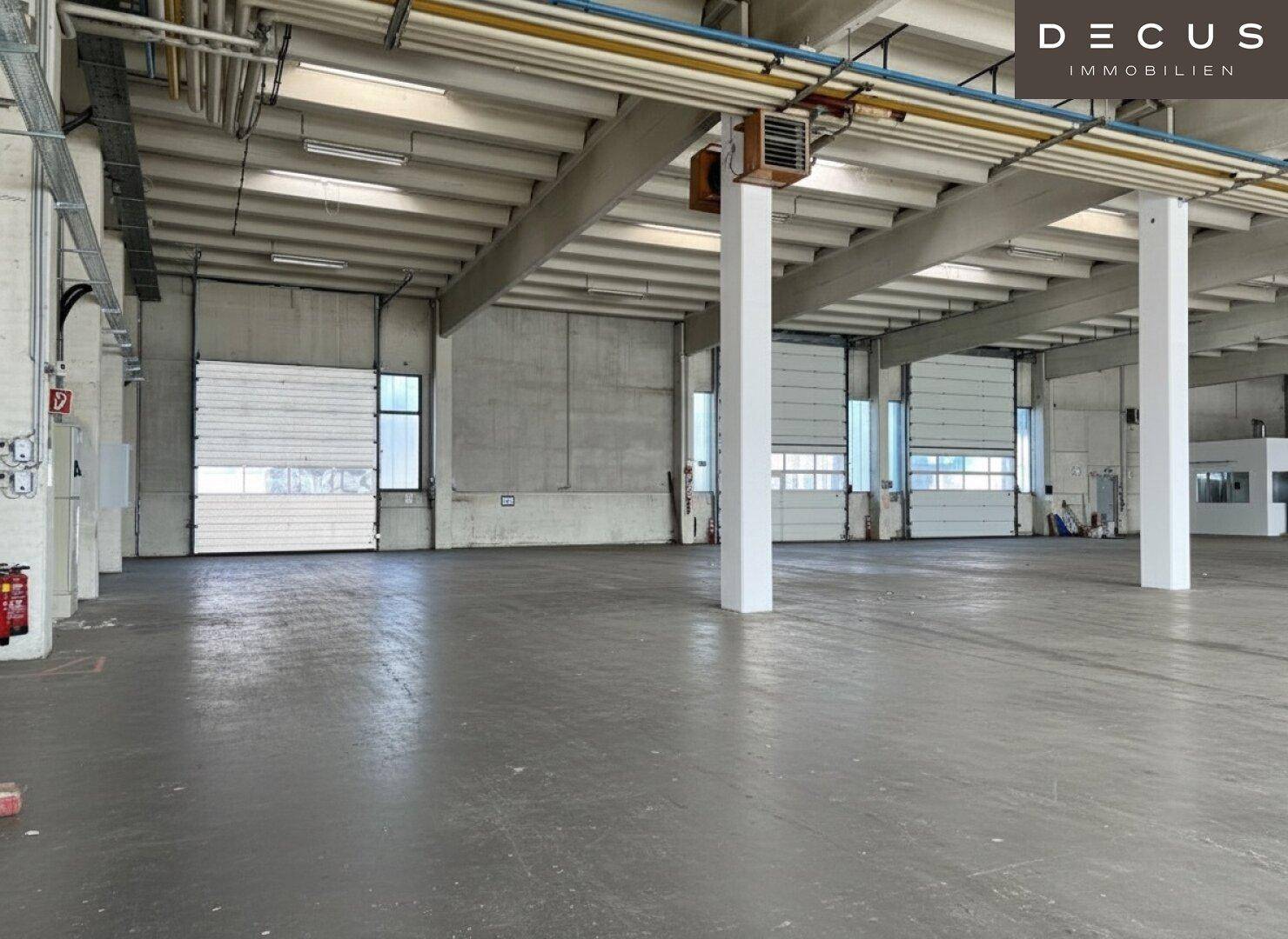 Geräumige Lagerhalle mit mehreren Rolltoren, Betonwänden und sichtbaren Installationen an der Decke.