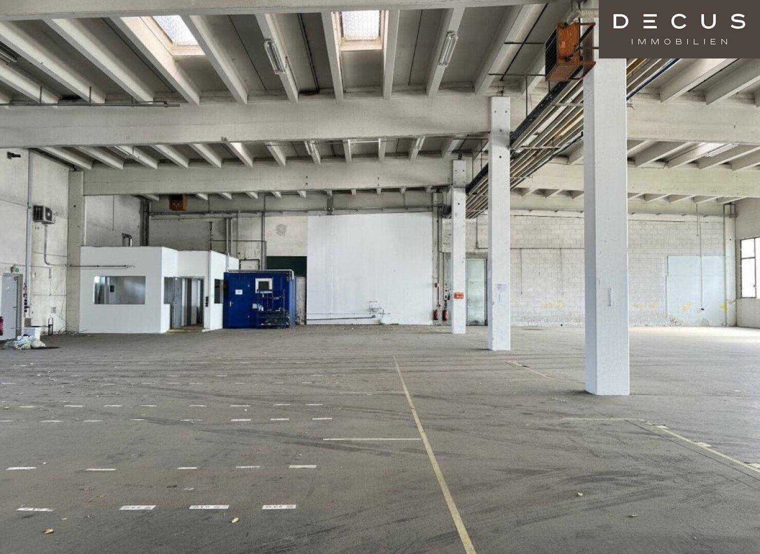 Weitläufige Lagerhalle mit Büroeinheiten, hohen Decken und Oberlichtern für natürliche Beleuchtung.