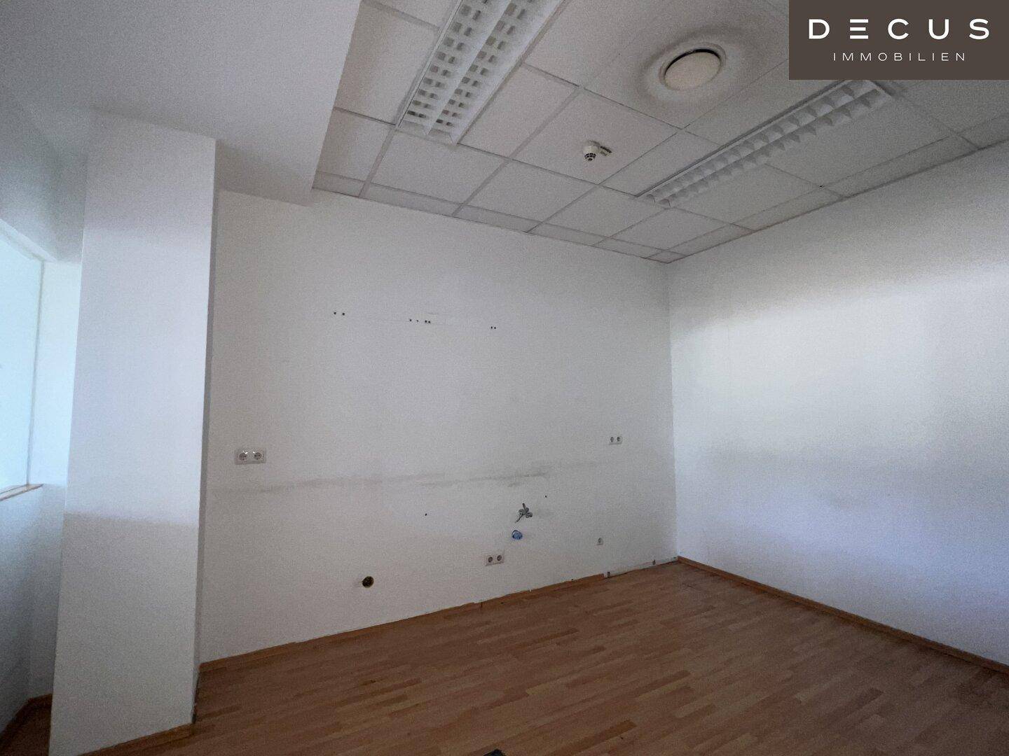 Leeres Büro mit Holzfußboden und einer Wand, die Gebrauchsspuren aufweist.