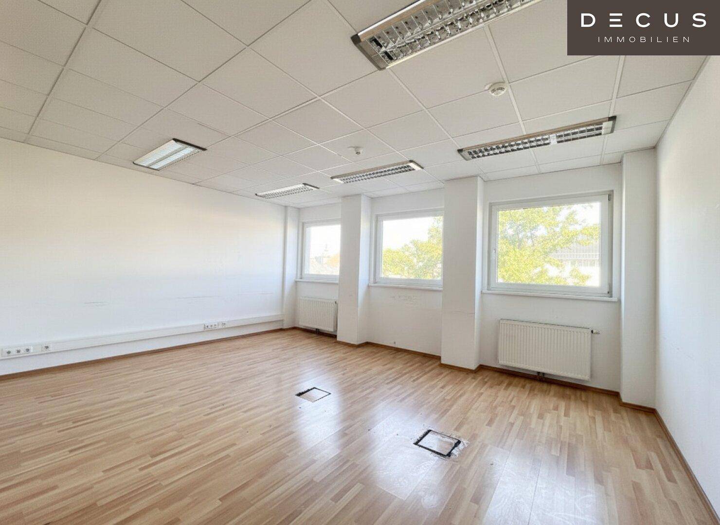 Geräumiges Büro mit mehreren Fenstern und praktischem Holzfußboden, ideal für Arbeitsbereiche.