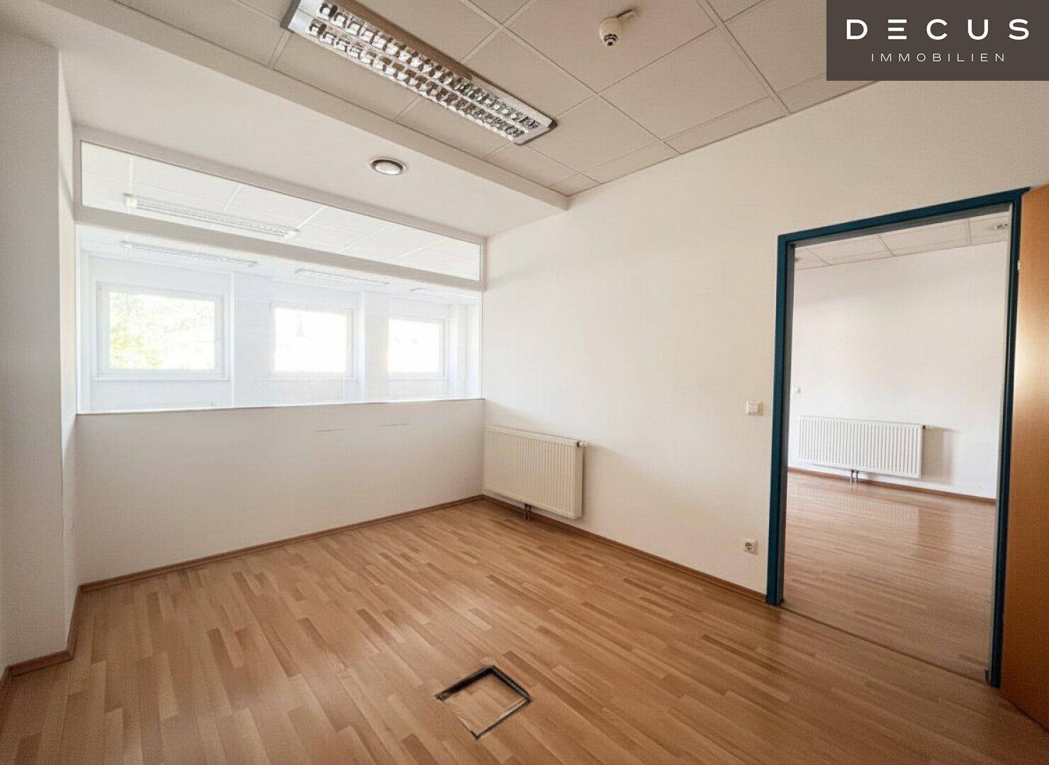 Büro mit Holzfußboden und einer Fensterfront, die den Raum mit natürlichem Licht erfüllt.