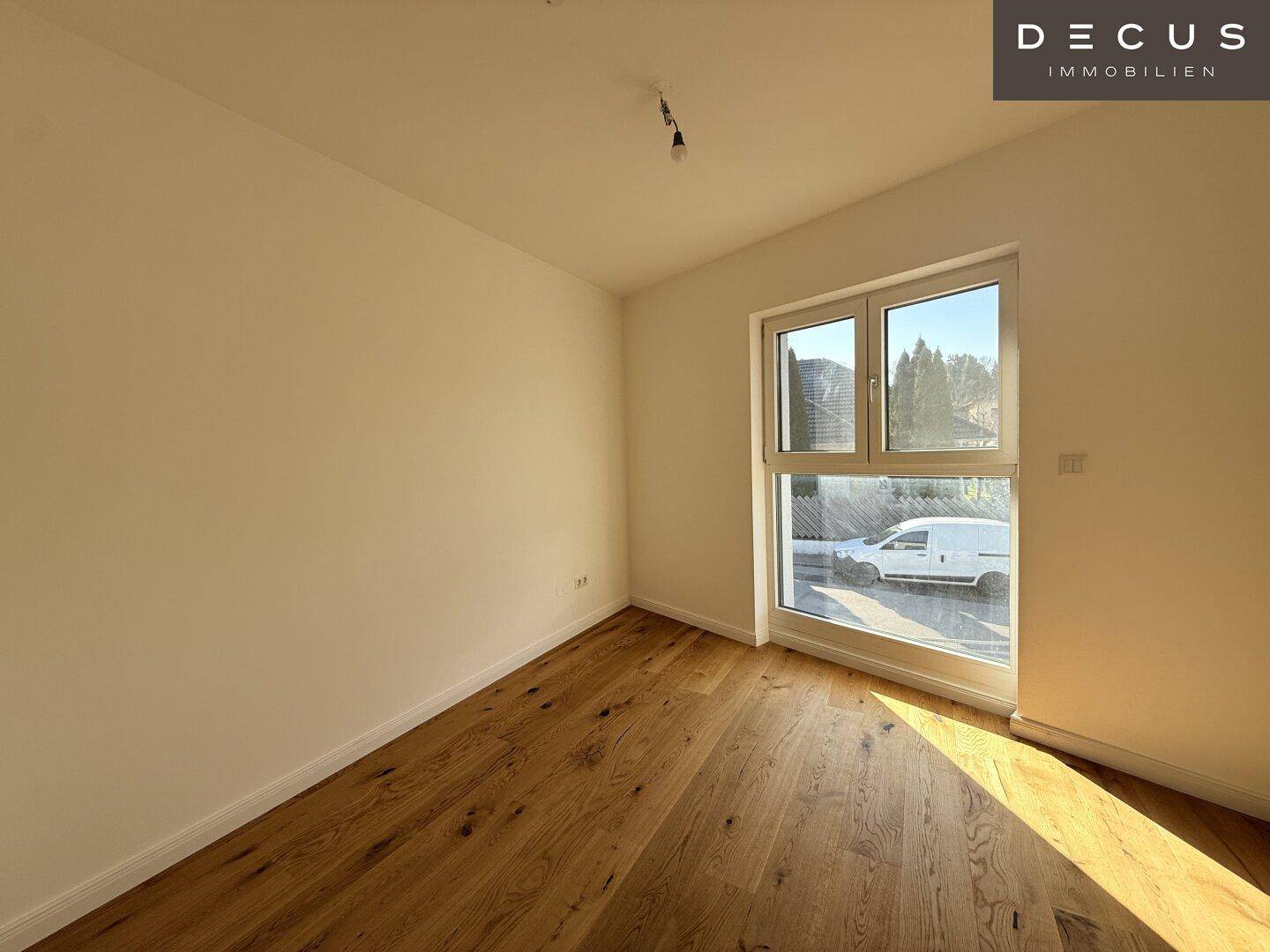 Helles Schlafzimmer mit Holzboden und großem Fenster, das viel Tageslicht hereinlässt.