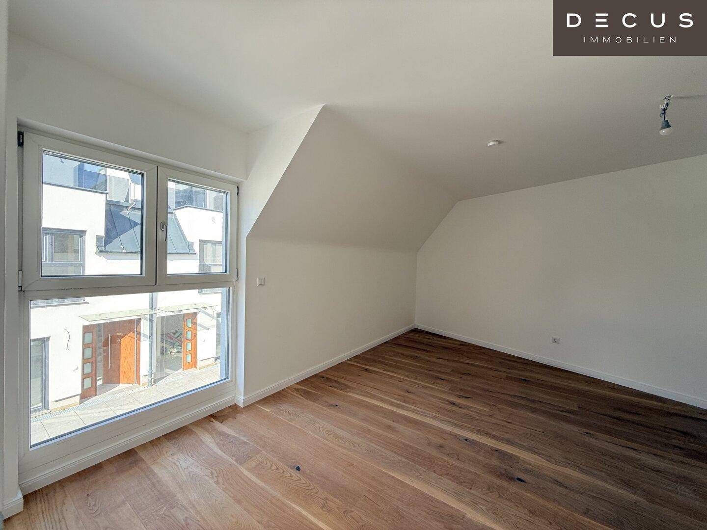 Heller Raum im Dachgeschoss mit Holzboden, großem Fenster und schräger Decke.