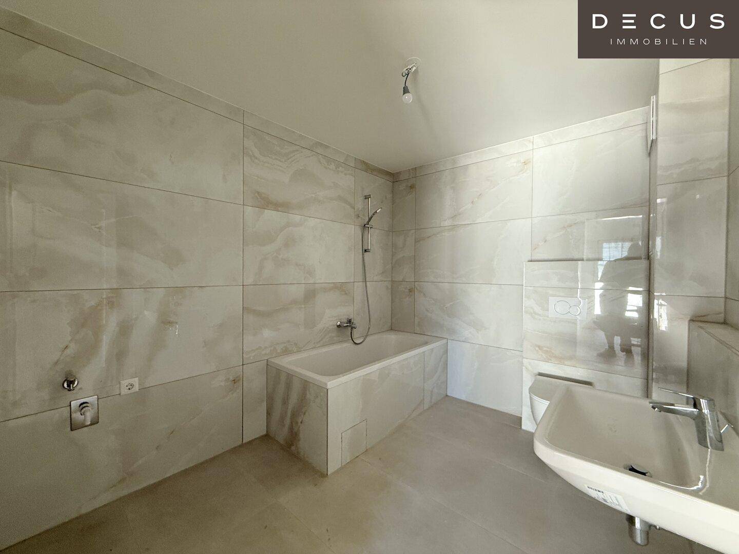 Modernes Badezimmer mit hellen Fliesen, Badewanne und Waschbecken, in neuwertigem Zustand.
