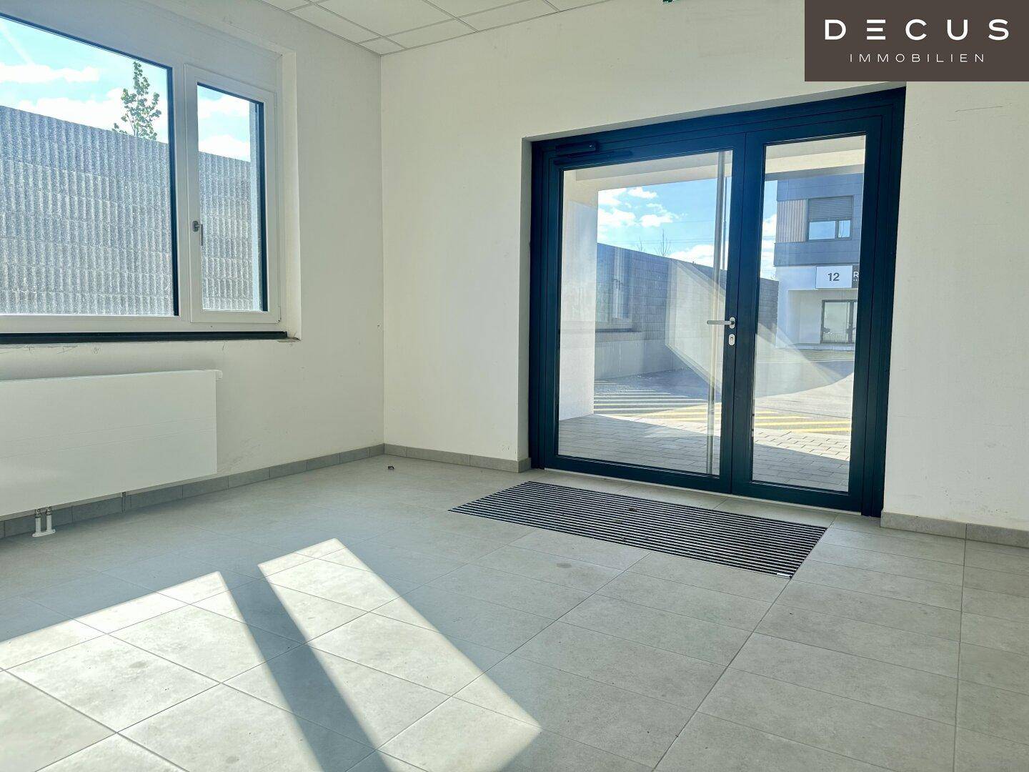 Heller Eingangsbereich mit Fliesenboden, großem Fenster und einer modernen Glastür.