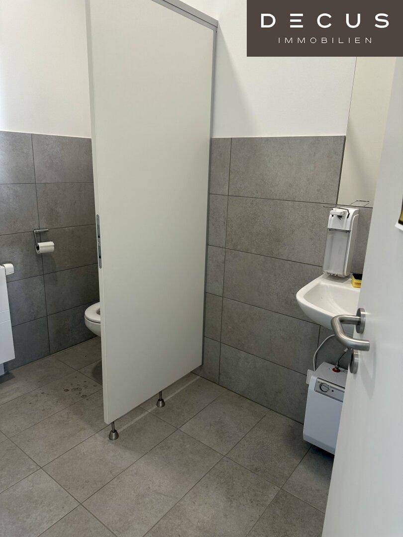 Modernes WC mit grauen Fliesen an Wänden und Boden, ausgestattet mit Waschbecken und Toilette.