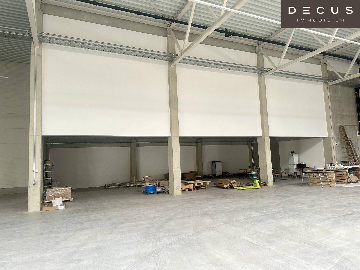 Innenbereich der Lagerhalle mit drei großen weißen Paneelen und gestapelten Paletten auf dem Betonboden.