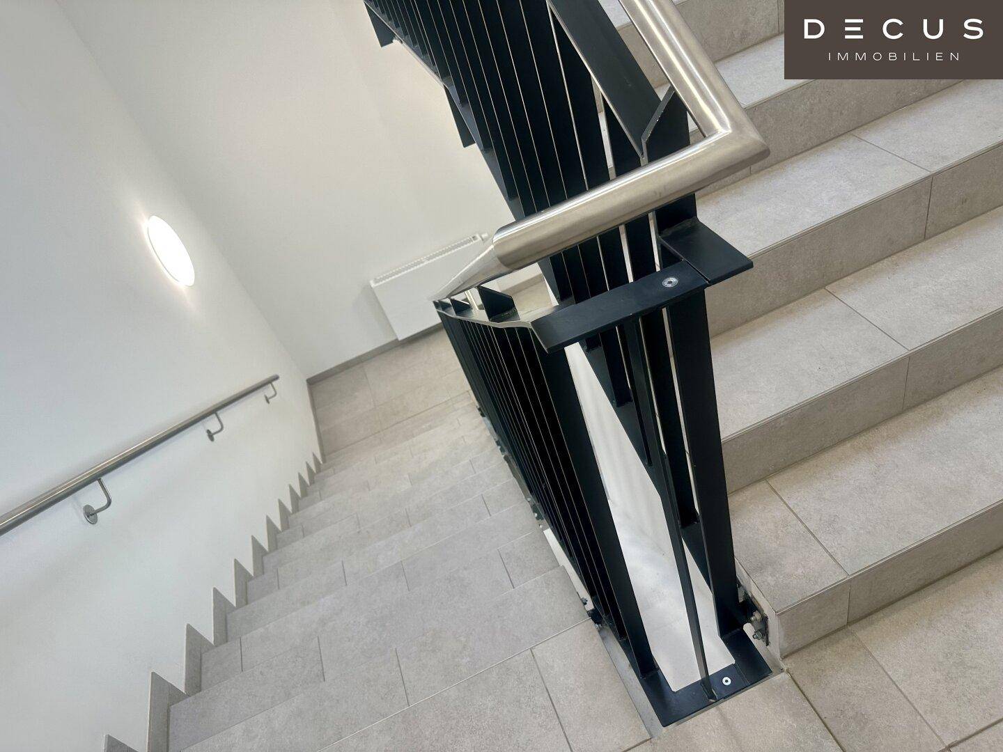 Modernes Treppenhaus mit grauen Fliesenstufen und einem eleganten schwarzen Metallgeländer mit Handlauf.