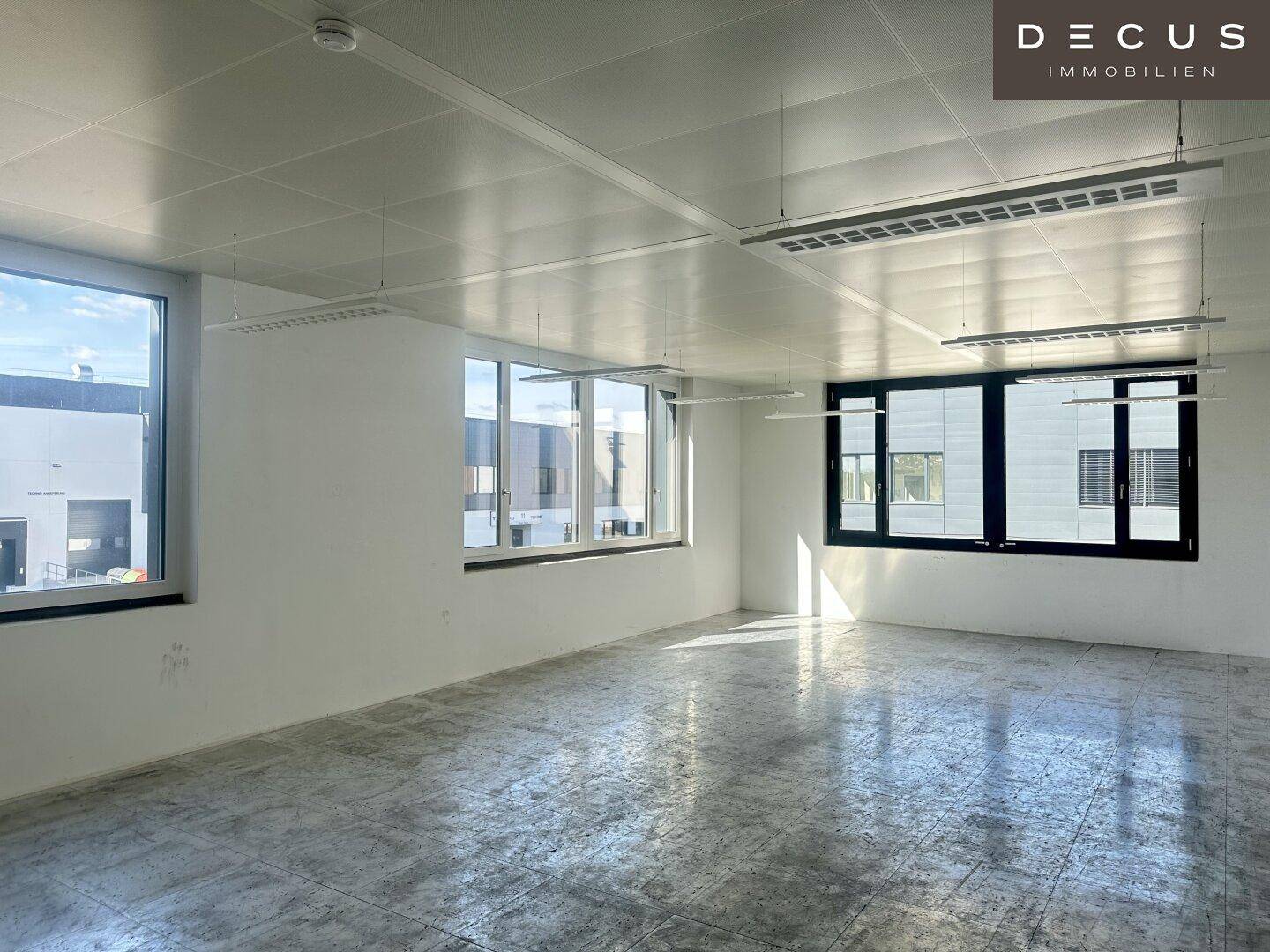 Großer, heller Büroraum im Rohbau mit Betonboden und vielen Fenstern für optimale Belichtung.