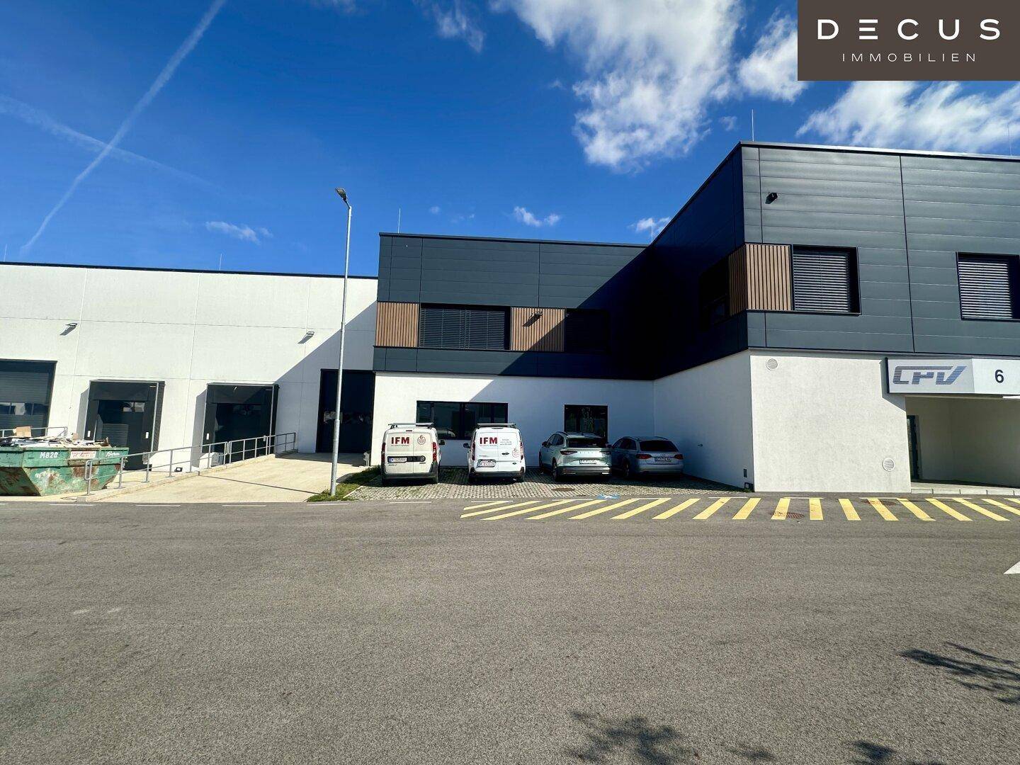 Moderne Gewerbeimmobilie mit dunkler Fassade, großen Fenstern und Parkplätzen im Außenbereich.