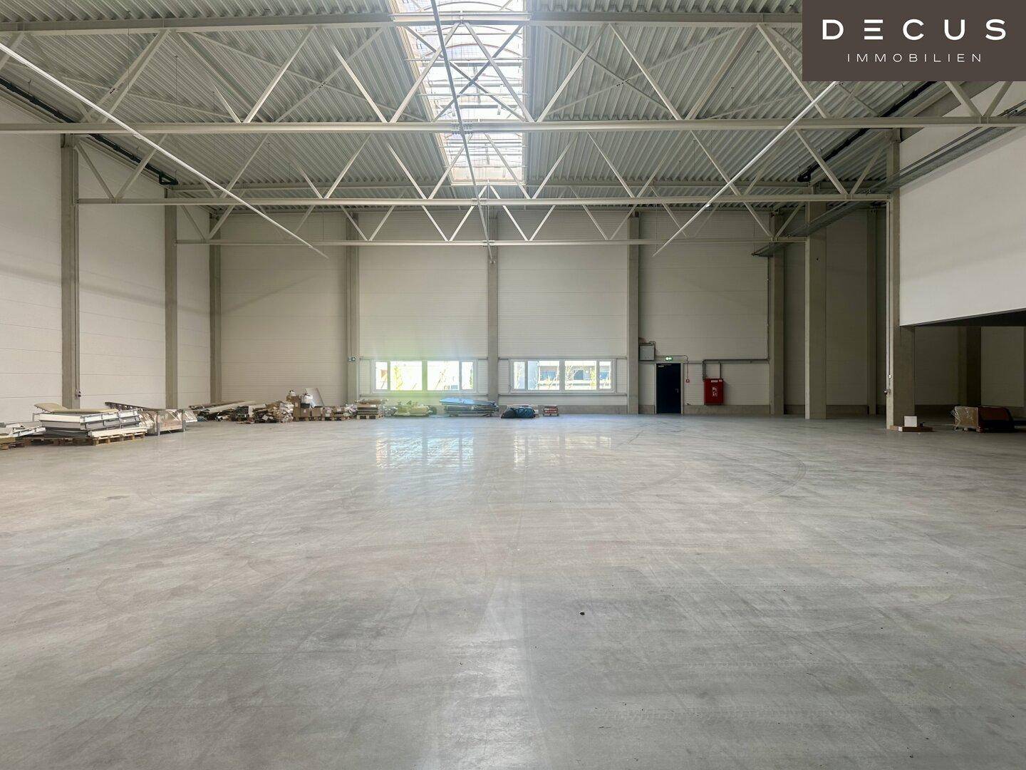 Helle und geräumige Lagerhalle mit Oberlichtern, Fenstern und einem glatten Betonboden.