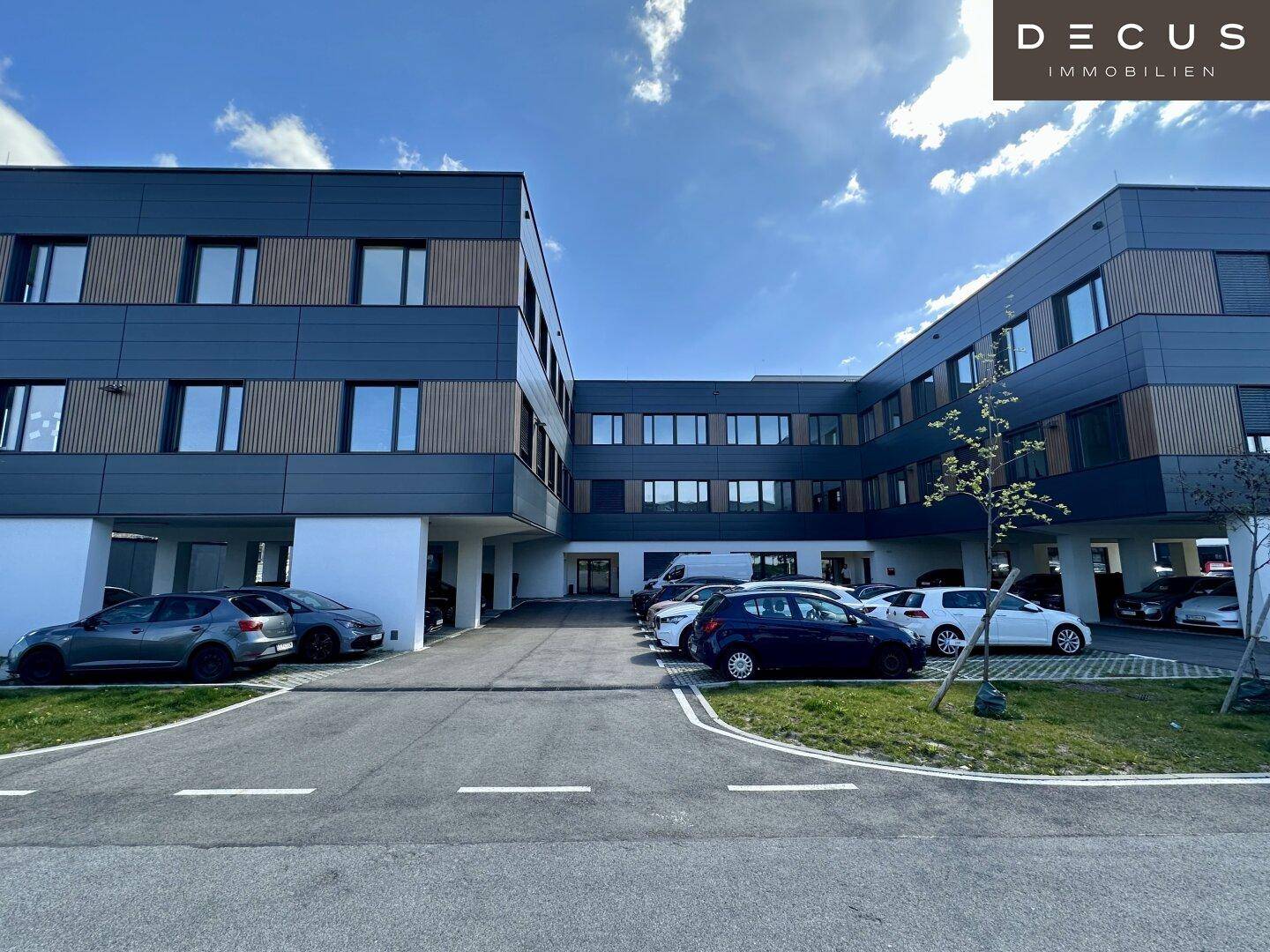 Modernes Gebäude mit dunkelgrauer Fassade und integrierten Parkplätzen im Freien und unter dem Gebäude.
