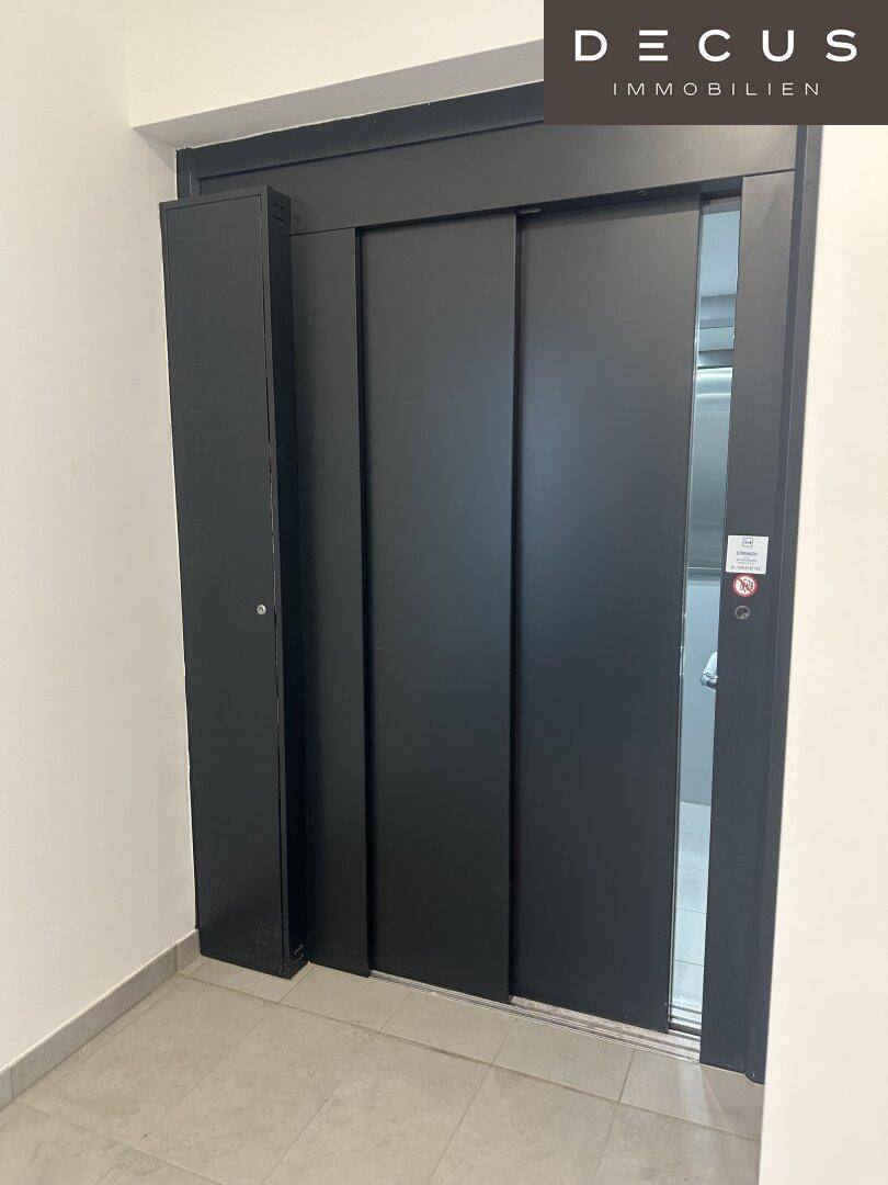 Moderner Aufzug mit schwarzen Türen in einem hellen Flur, bereit zur Nutzung in einem Geschäftsgebäude.