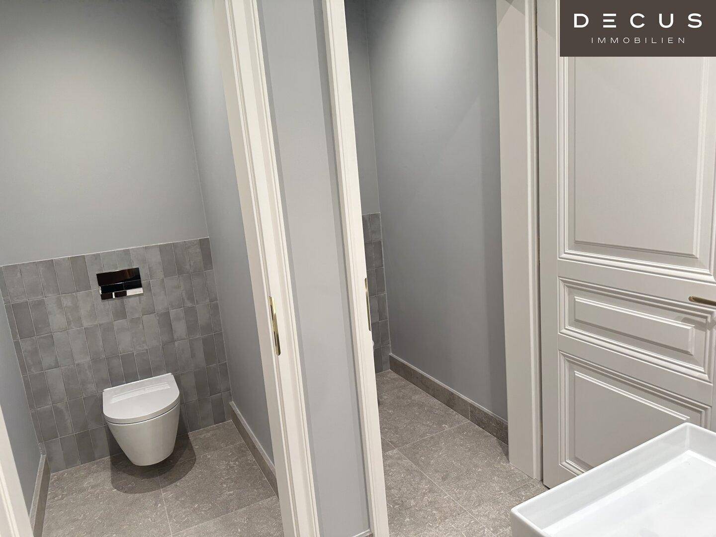 Separate Toilettenkabinen mit modernen Wand-WCs und grauen Fliesen, in einem frisch renovierten Bereich.