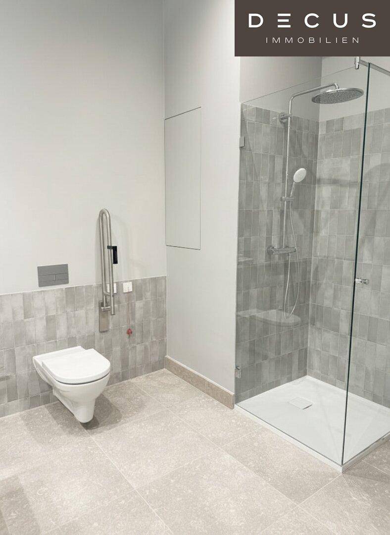 Modernes Badezimmer mit ebenerdiger Dusche, Wand-WC und grauen Fliesen, barrierefrei ausgestattet.
