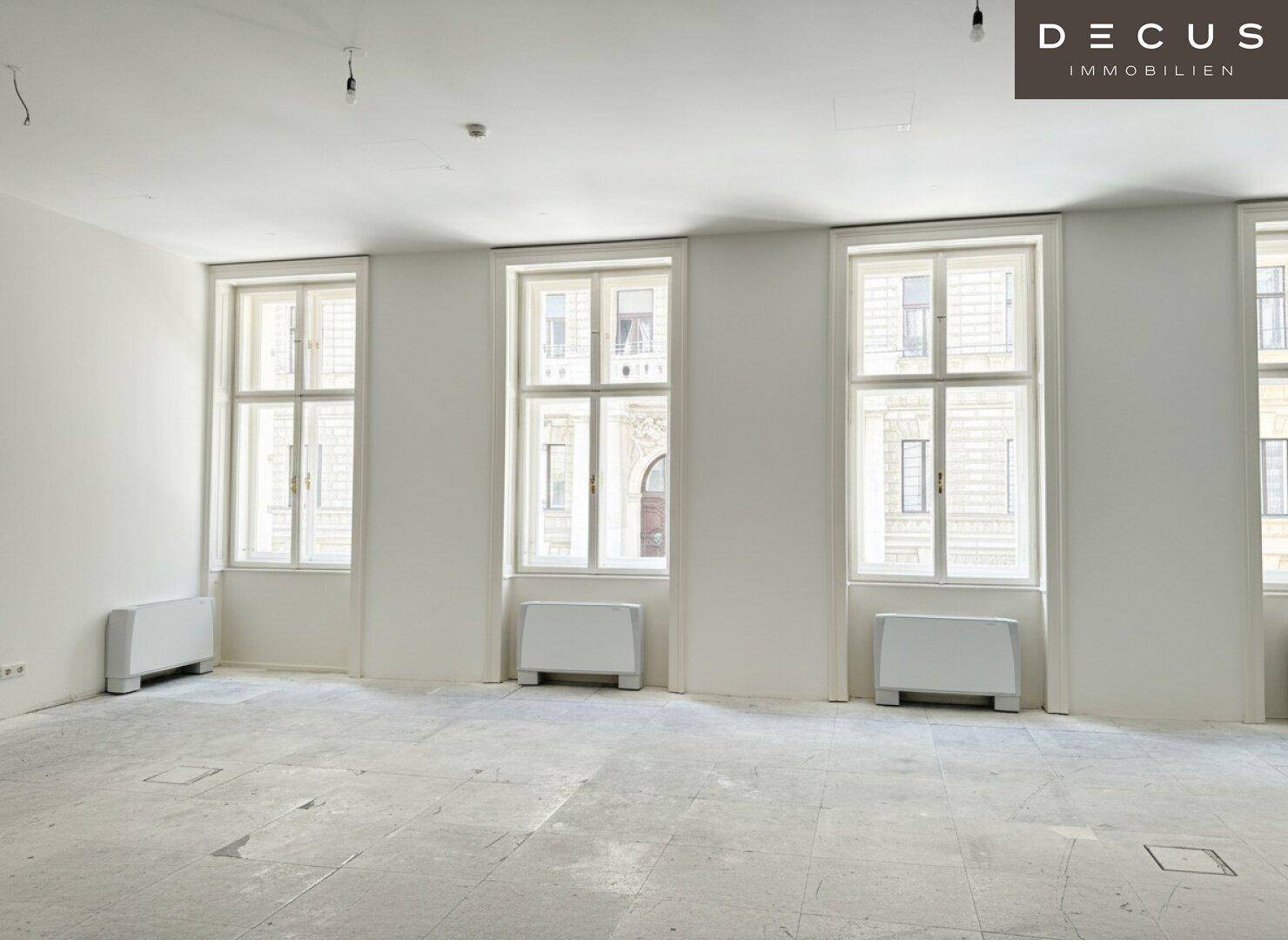 Helle Fensterfront in einem großen Raum mit Heizkörpern unter den hohen Fenstern und hellem Boden.