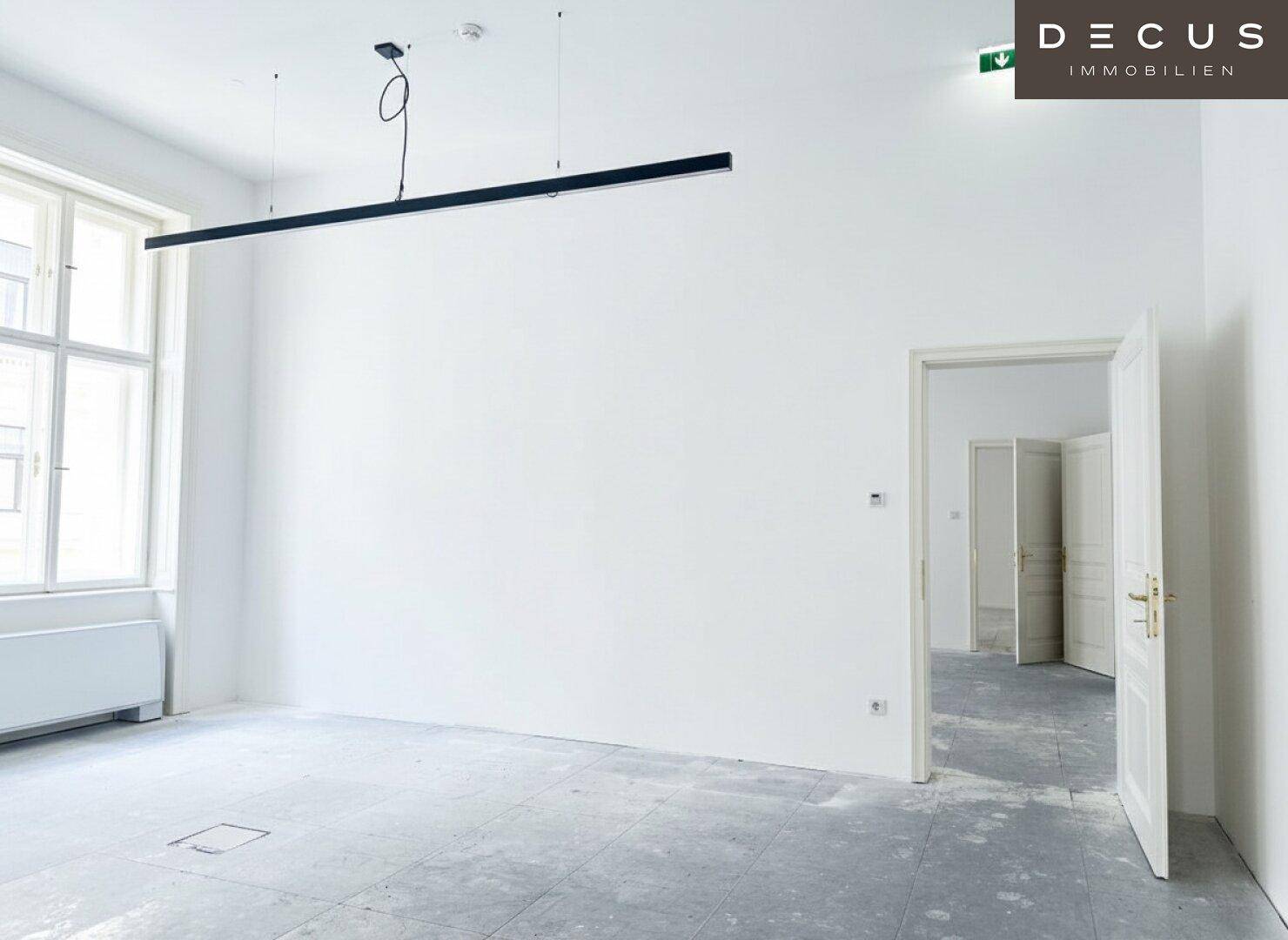 Geräumiger, heller Raum mit einer modernen Deckenleuchte und mehreren Türen, ideal für Büros.