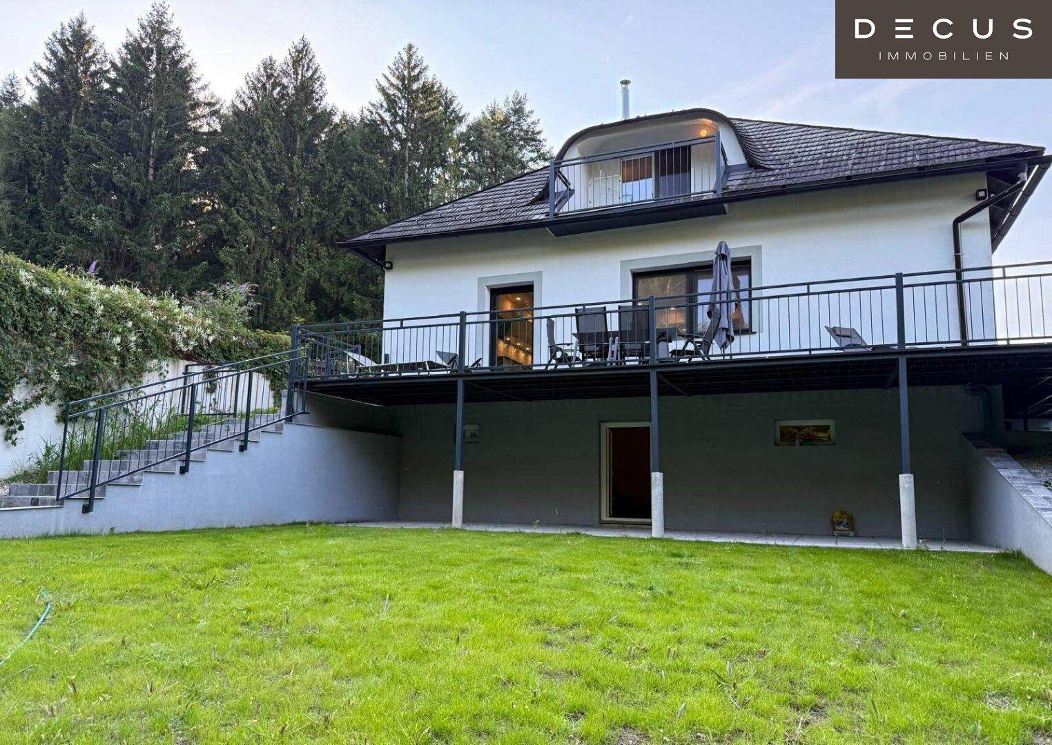 Hinteransicht des Hauses mit weitläufigem Rasen und erhöhter Terrasse.
