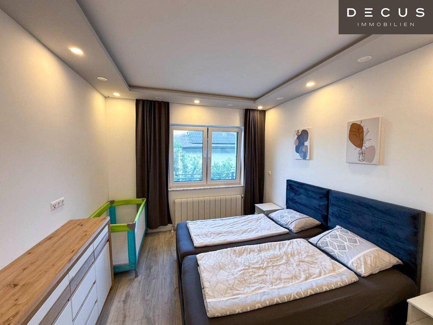 Helles Schlafzimmer mit zwei Betten, Holzkommode und Blick nach draußen.
