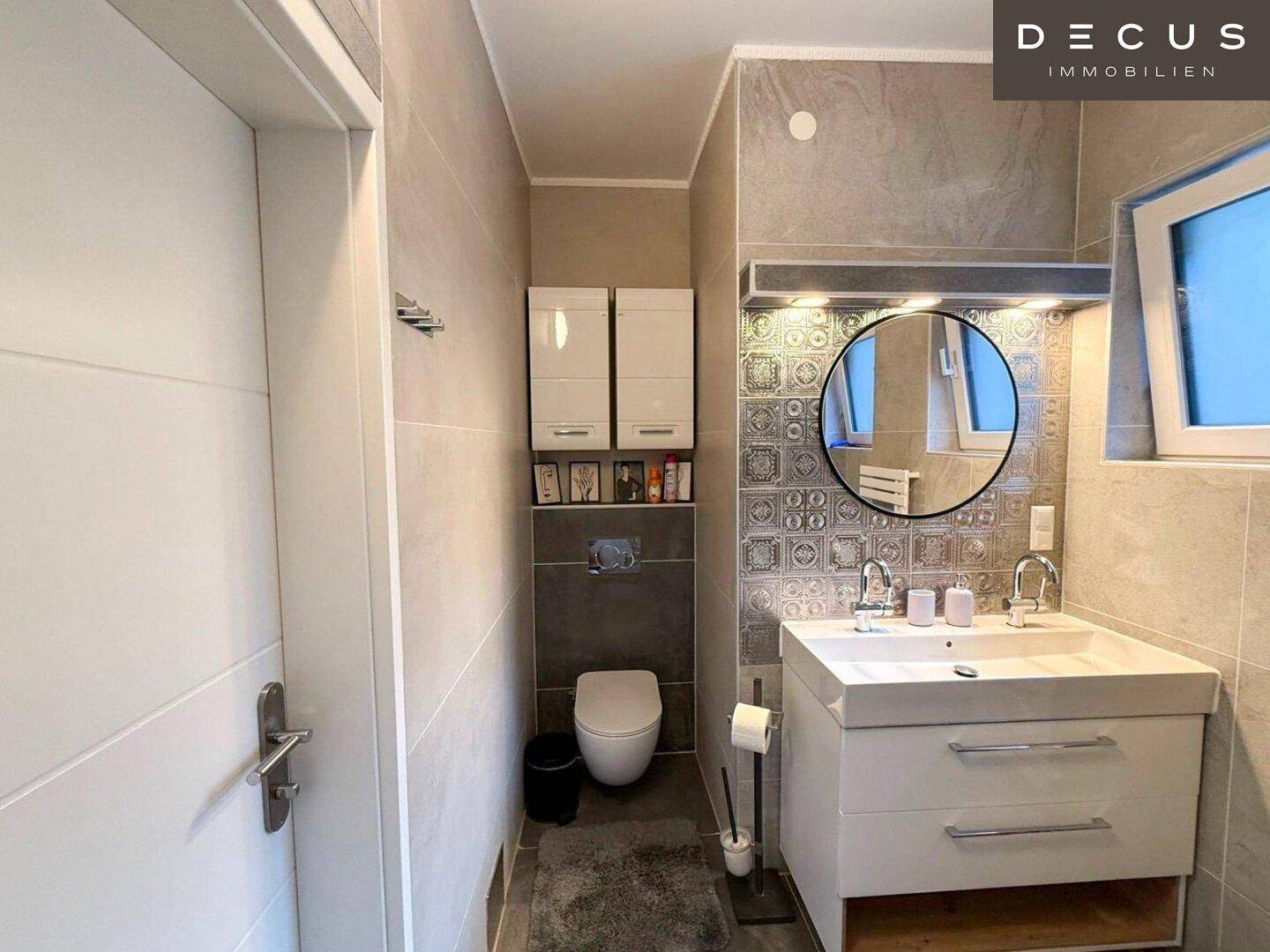 Modernes Badezimmer mit Waschtisch, Wand-WC und Fliesen in Grautönen.