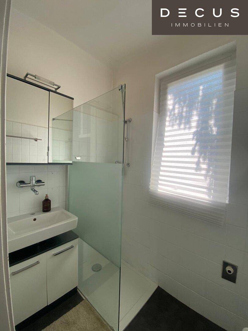 Modernes Badezimmer mit Duschkabine aus Glas, Waschbecken und einem Fenster für Tageslicht.