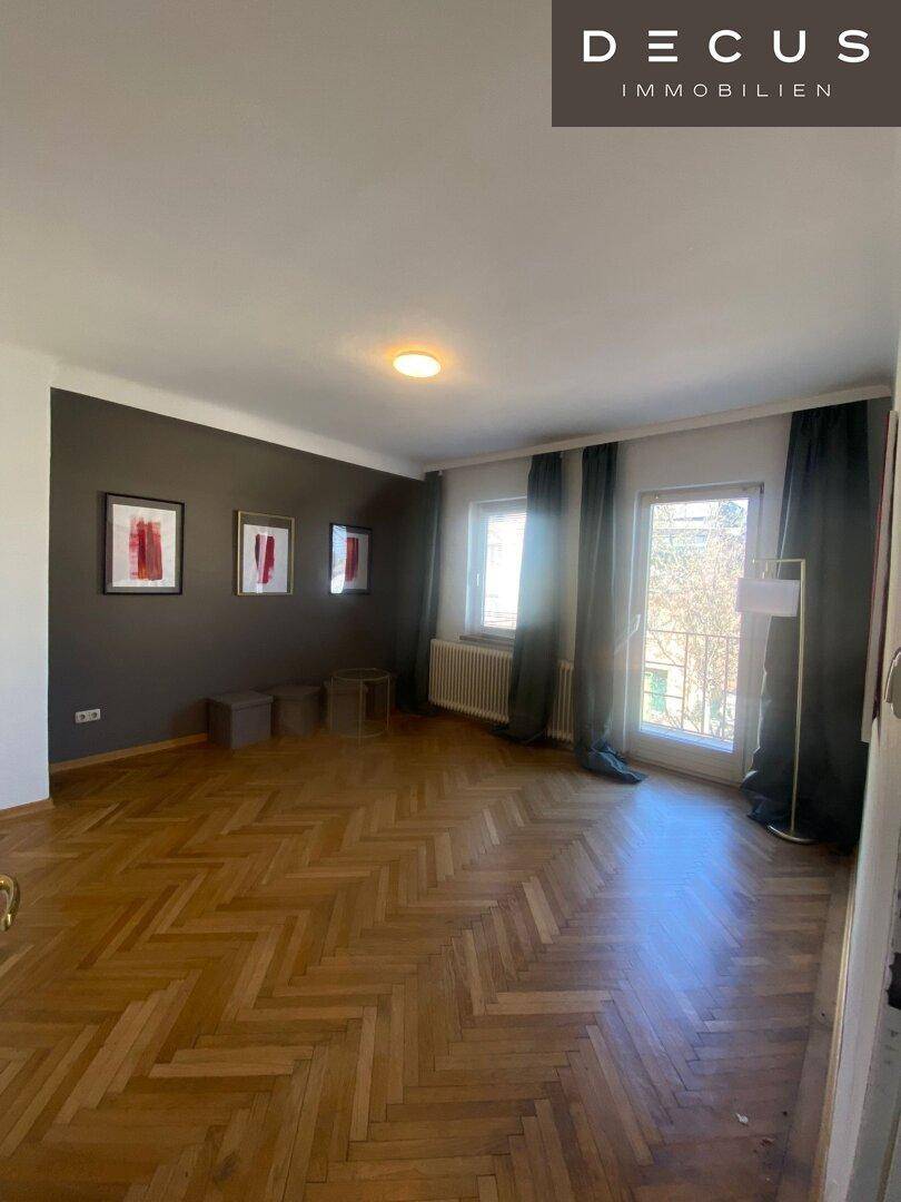 Geräumiges Wohnzimmer mit Fischgrätparkett, dunkler Akzentwand und Zugang zum französischen Balkon.