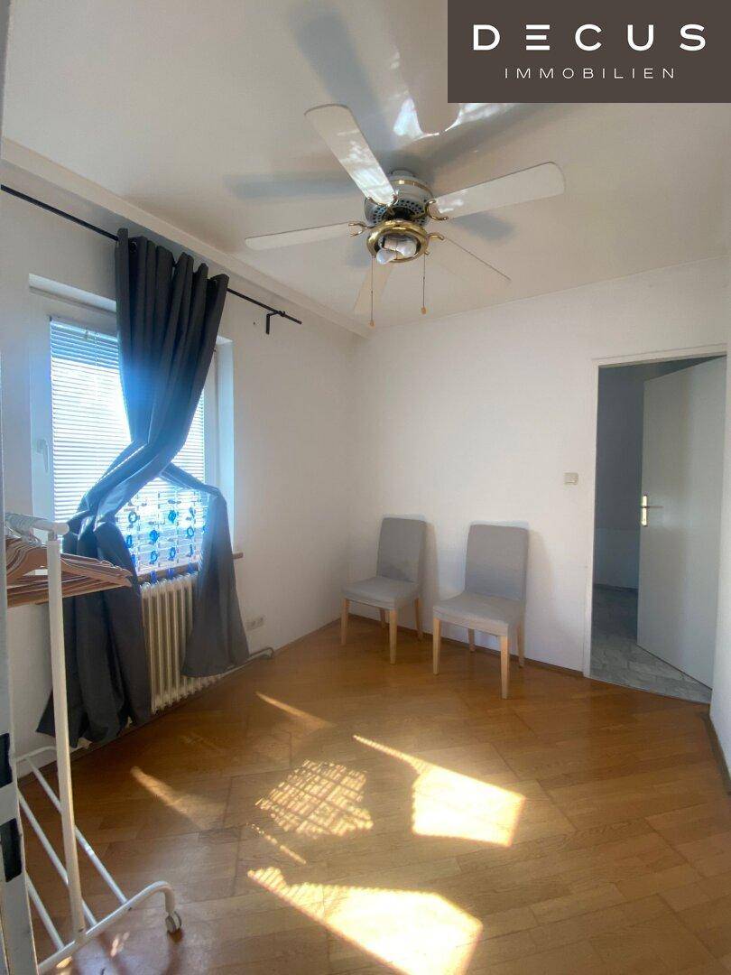 Helles Schlafzimmer mit Holzboden, Deckenventilator und Fenster mit Jalousien.