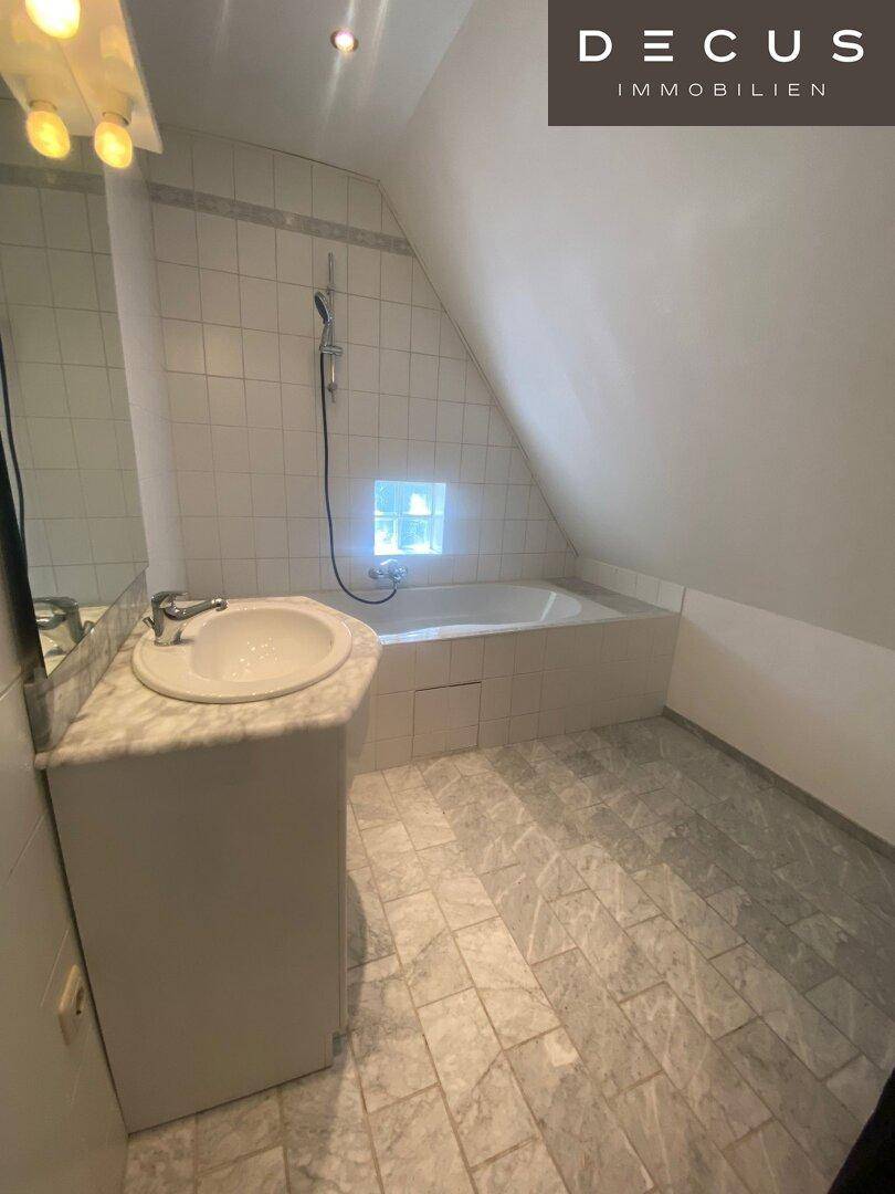Badezimmer im Dachgeschoss mit Badewanne, Waschbecken und schrägen Wänden.