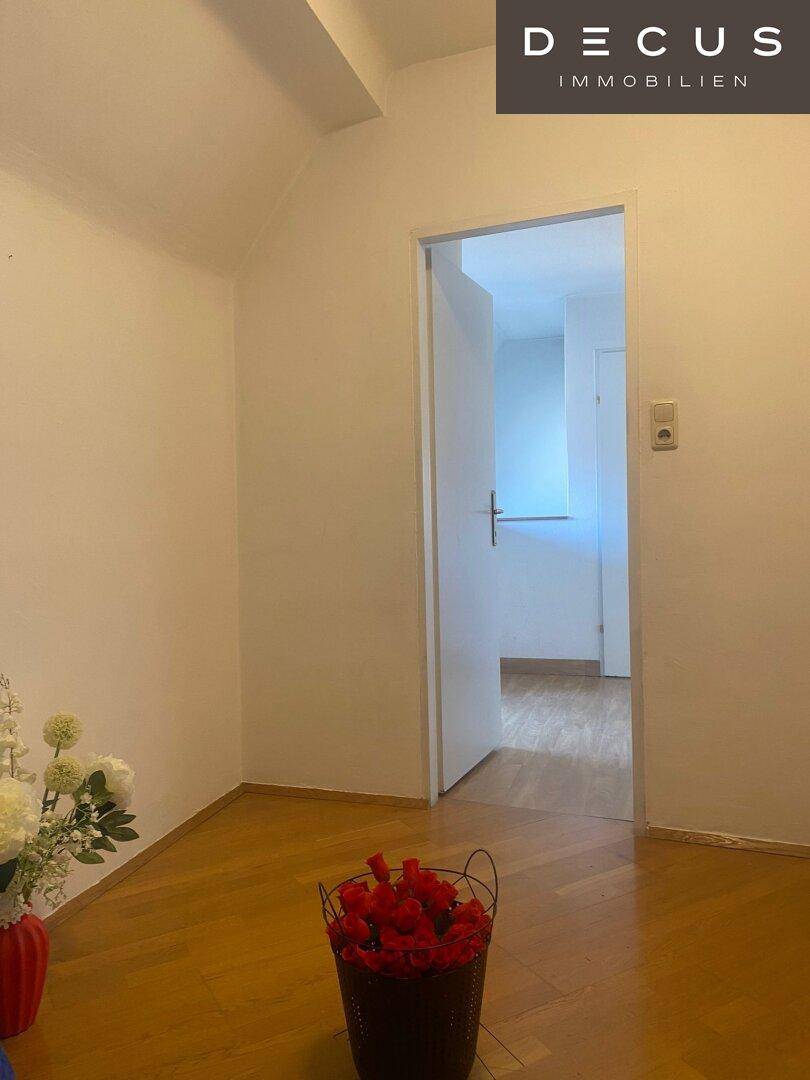 Heller Innenraum mit Holzboden und offener Tür, die zu einem weiteren Zimmer führt.