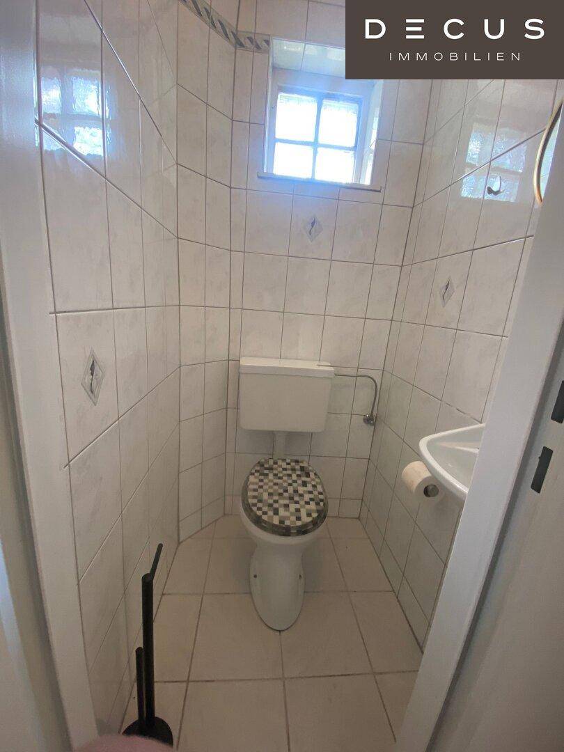 Gefliestes Gäste-WC mit Toilette, Waschbecken und einem kleinen Fenster.