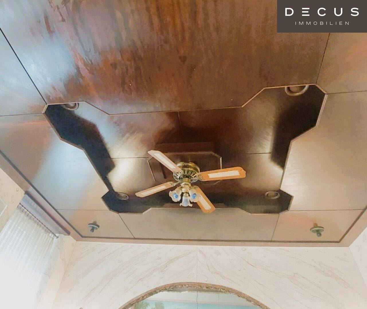 Eine detailreiche Decke mit Holzpaneelen und einem Deckenventilator, der zur Belüftung des Raumes dient.