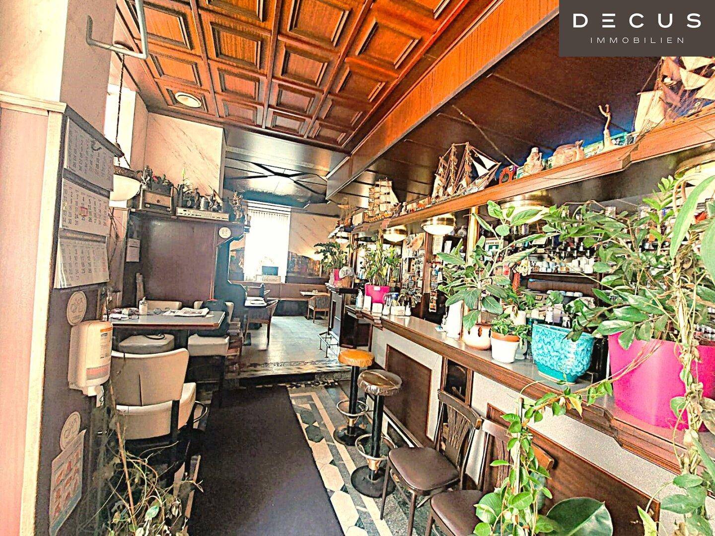 Eine lange Bar mit Holztheke, vielen Pflanzen und dekorativen Elementen, die sich durch den Raum zieht.