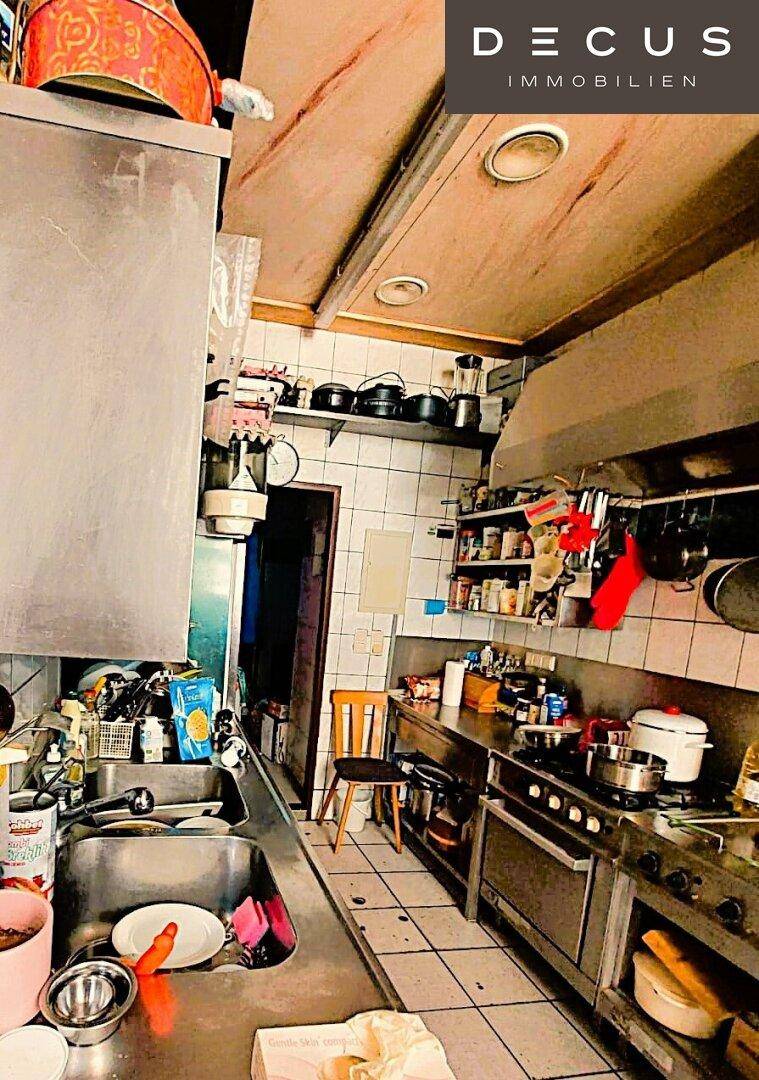Eine professionelle Küche mit Edelstahlspüle, Arbeitsflächen und Regalen voller Kochutensilien, bereit für den Einsatz.