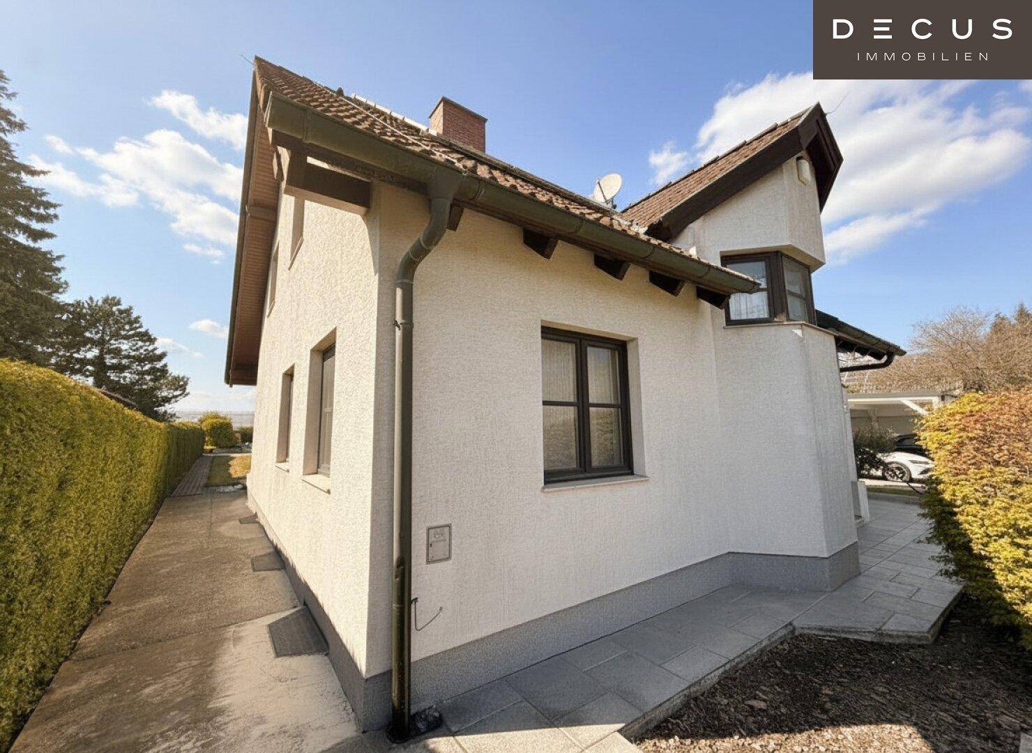 Seitenansicht des Hauses mit gepflastertem Weg, Hecke und Blick in die Ferne.