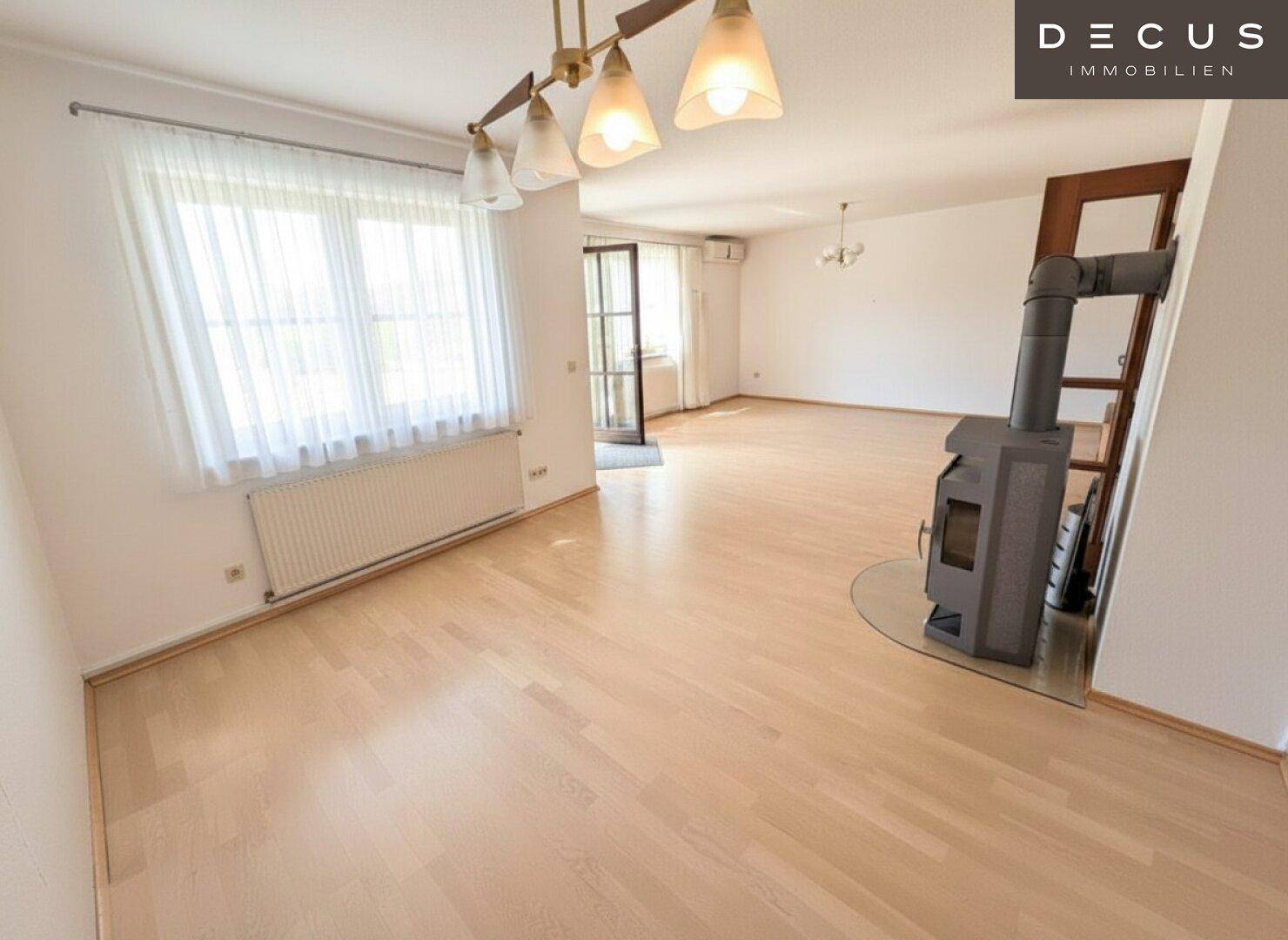 Geräumiges Wohnzimmer mit hellem Holzboden, Kaminofen und Zugang zum Außenbereich.