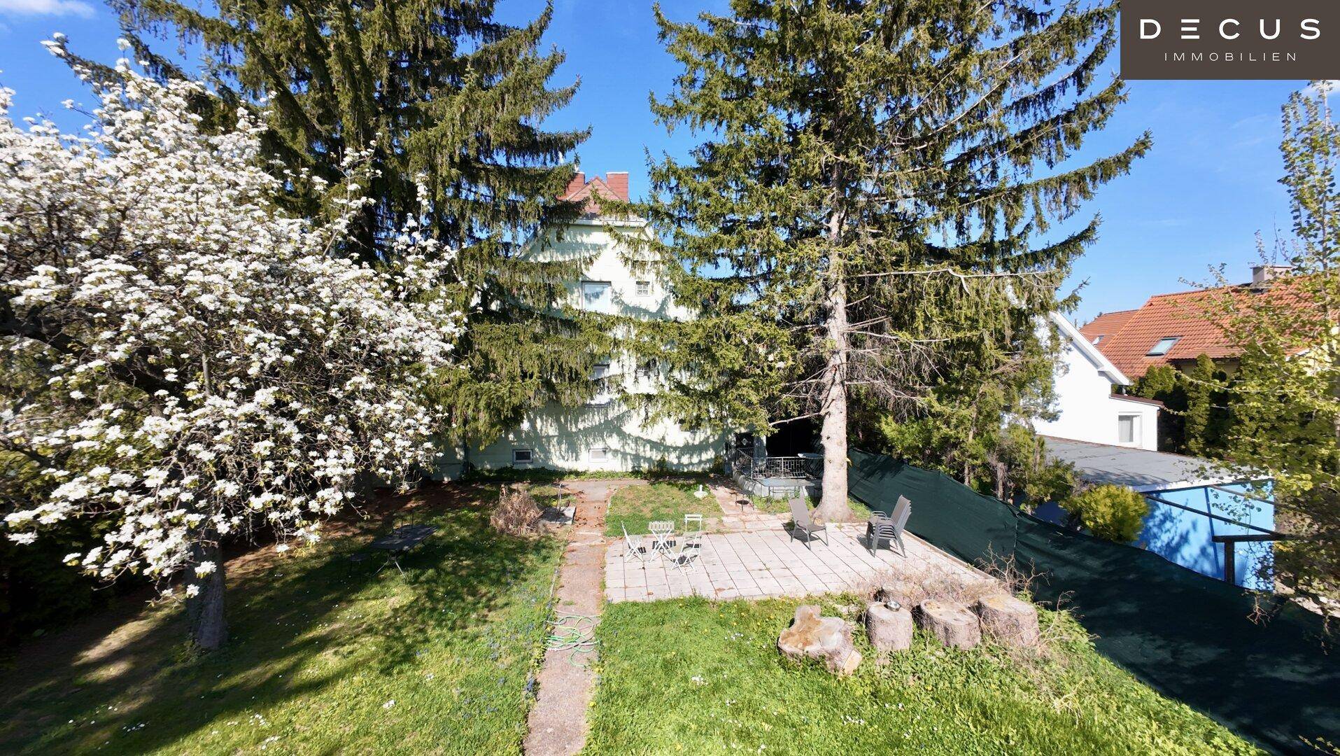 Großer Garten mit Rasenfläche, Bäumen und einer gepflasterten Terrasse für Sitzgelegenheiten.