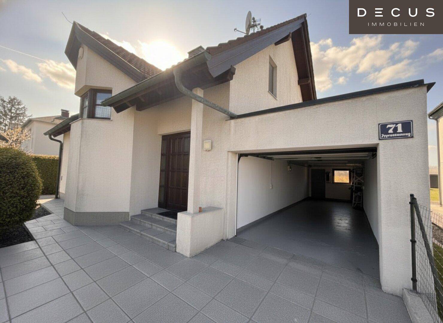 Einfamilienhaus mit offener Garage und gepflasterter Zufahrt unter strahlend blauem Himmel.