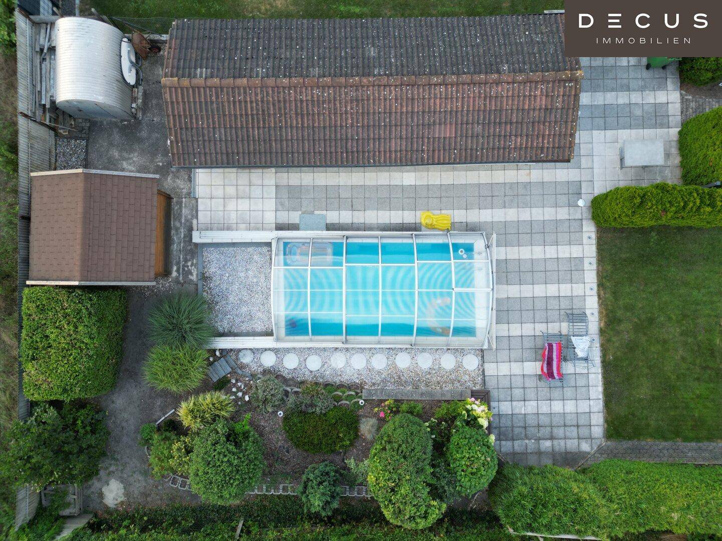Luftaufnahme des Hinterhofs mit überdachtem Pool, großer Terrasse und Gartenhaus.