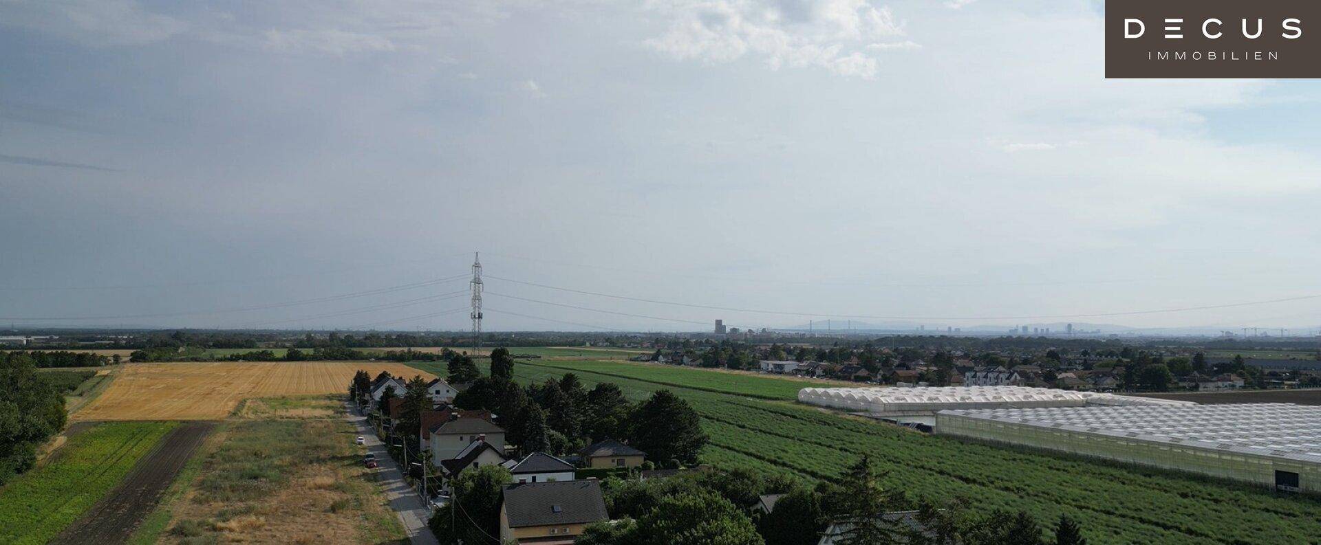 Luftaufnahme einer ländlichen Gegend mit Wohnhäusern, Feldern und großen Gewächshäusern.